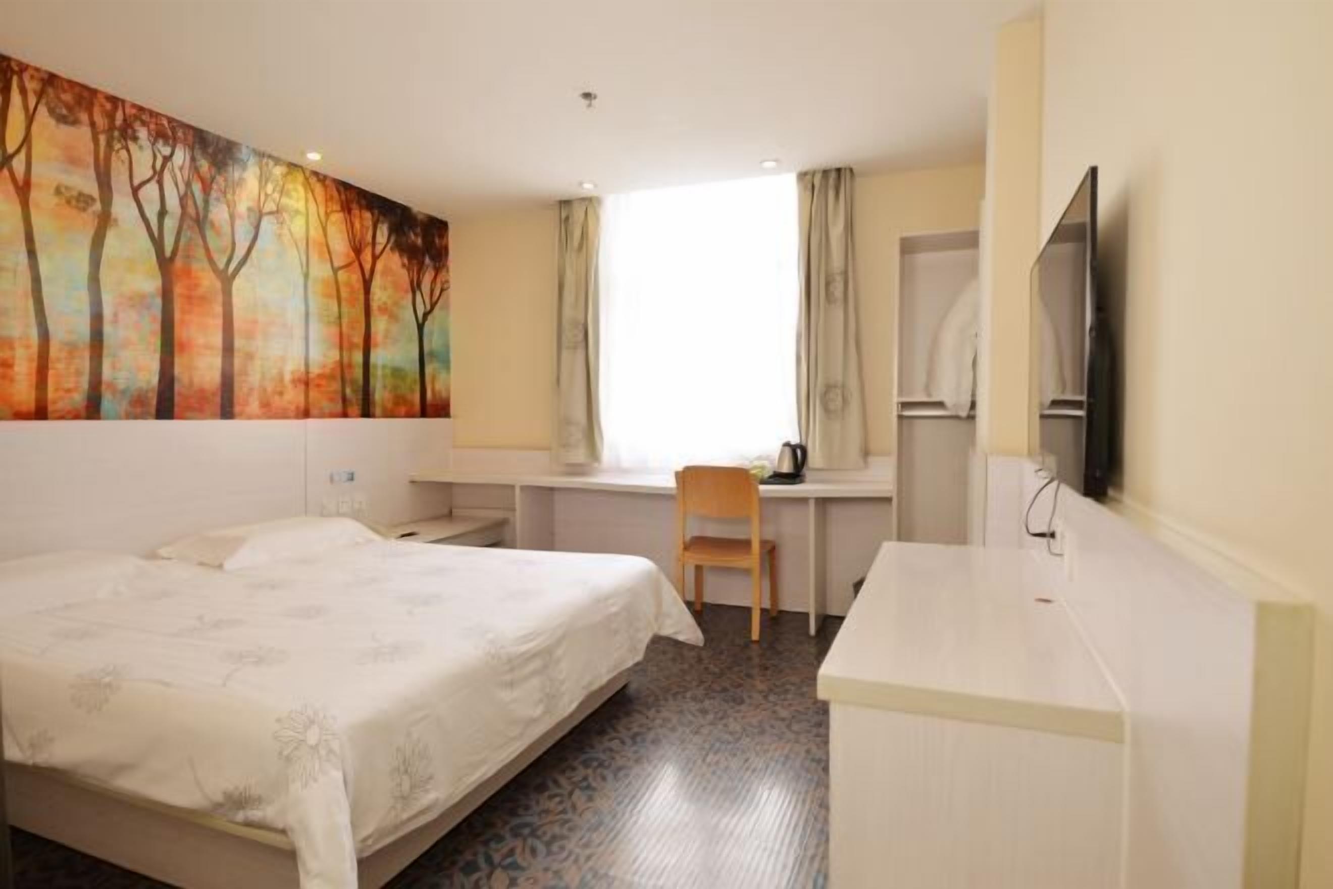 A hotel room with a bed, a desk, a chair, a television, and a painting on the wall.