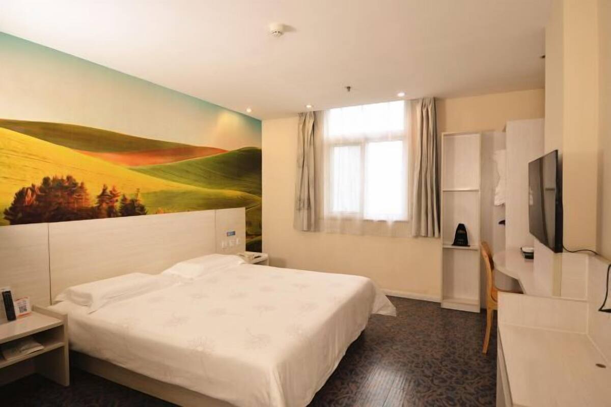Ein Hotelzimmer mit einem Bett, einem Schreibtisch, einem Stuhl, einem Fernseher, einem Gemälde und einem Fenster mit Vorhängen.