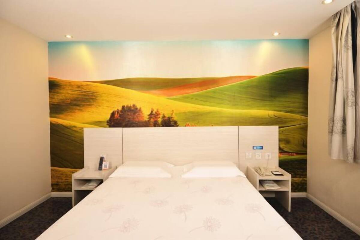 Ein Hotelzimmer mit einem großen Bett, zwei Nachttischen, einem Beistelltisch und einer Wandmalerei von sanften Hügeln.