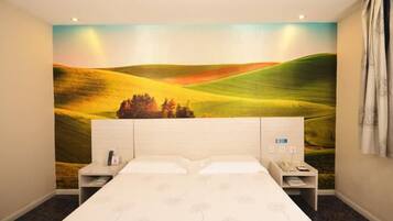 A hotel room with a large bed, two bedside tables, a nightstand, and a wall mural of rolling hills.
