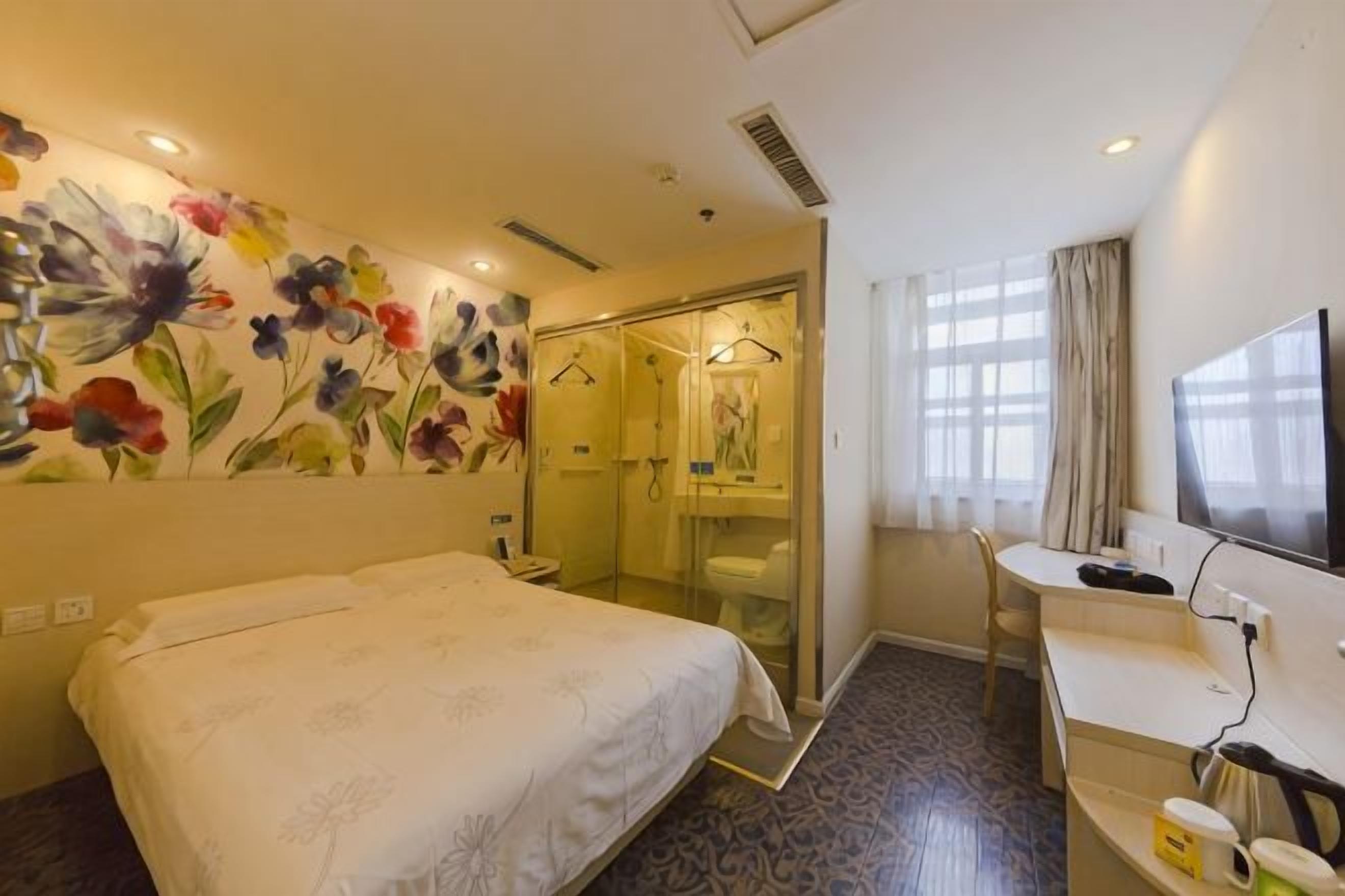 Quarto de hotel com cama, escrivaninha, chuveiro e um grande mural floral na parede.