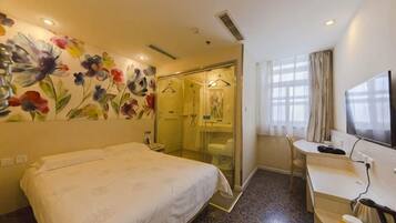 Quarto de hotel com cama, escrivaninha, chuveiro e um grande mural floral na parede.