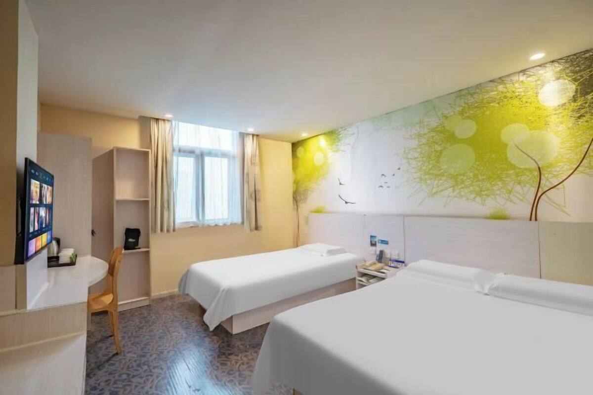 Ein Hotelzimmer mit zwei Betten, einem Schreibtisch, einem Stuhl, einem Bücherregal und einem großen Fenster.
