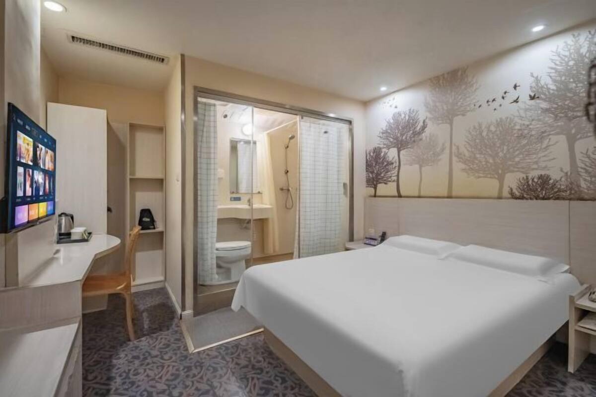 Ein Hotelzimmer mit Bett, Schreibtisch, Duschbereich und Fernseher auf dem Schreibtisch.