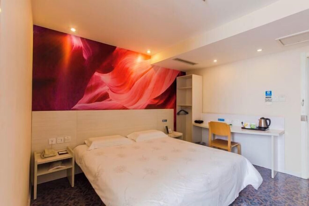 A hotel room with a bed, a desk, a chair, and a large abstract wall mural.