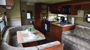 A compact RV kitchen with a dining area, including a microwave, sink, and stove. - Casa Coqui Camper, with WiFi, & AC, 3 miles from Falls Creek Falls State Park (Pikeville)