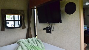 A room with a bed, a window, a television mounted on the wall, and a door leading to another room. - Casa Coqui Camper, with WiFi, & AC, 3 miles from Falls Creek Falls State Park (Pikeville)