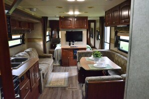 A compact RV interior with a kitchenette, a dining area, and a TV mounted on the wall. - Casa Coqui Camper, with WiFi, & AC, 3 miles from Falls Creek Falls State Park (Pikeville)