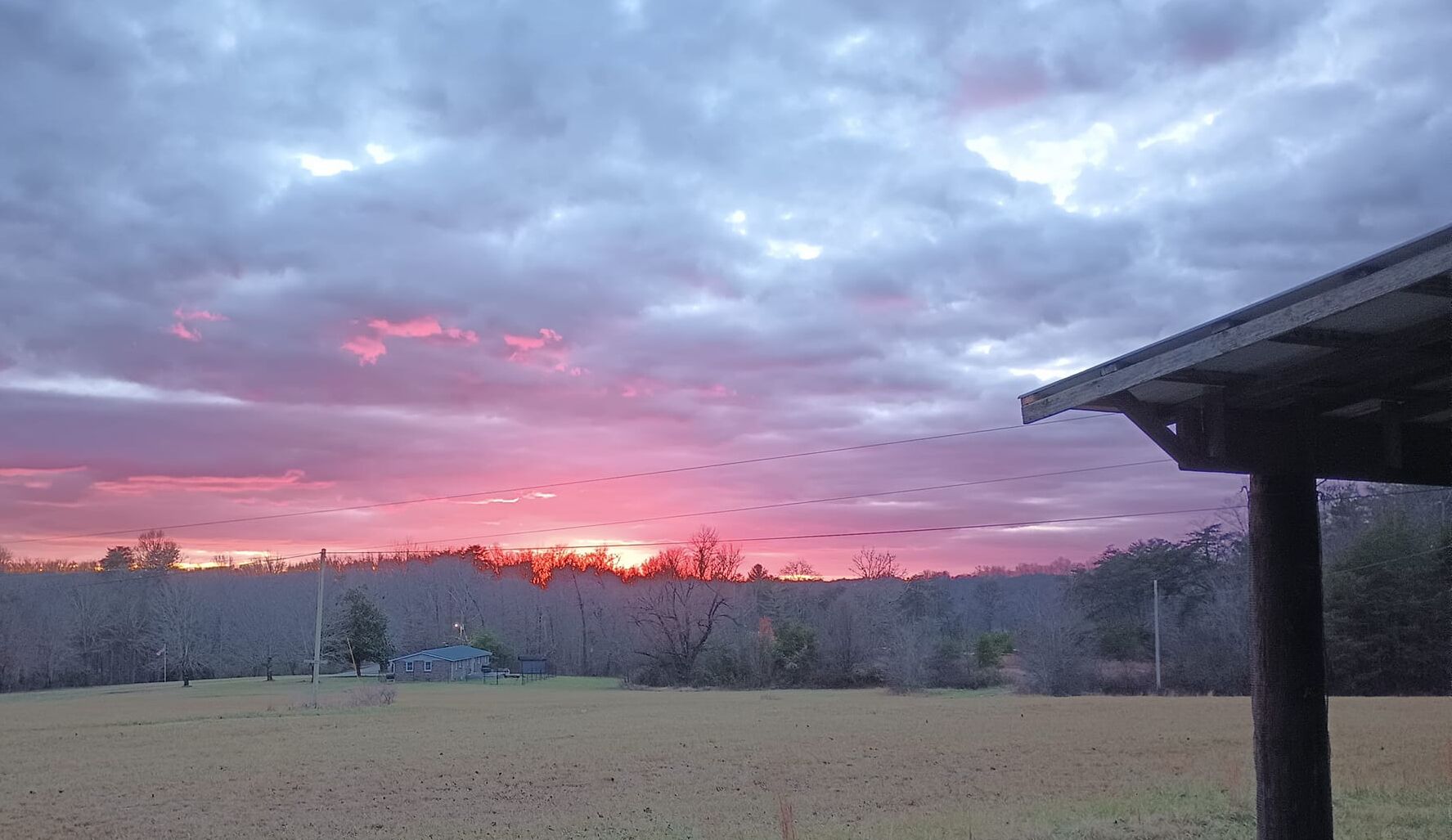 A sunset over a rural landscape with a wooden structure in the foreground.