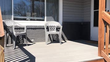 A covered outdoor area with a wooden deck, a table with chairs, and a window with blinds.