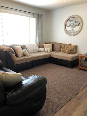 A living room with a sectional sofa, a leather ottoman, and a round wall decoration. - Park Place Your Comfortable Stay (Hutchinson)