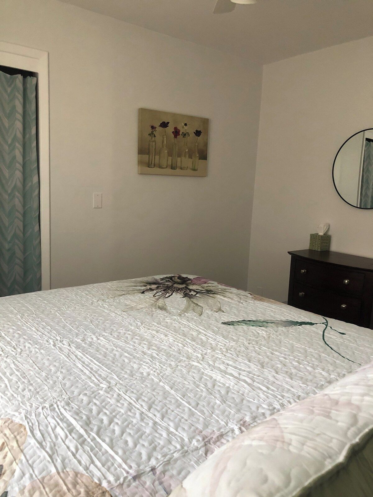 A bedroom with a bed, a painting on the wall, a dresser, and a mirror.