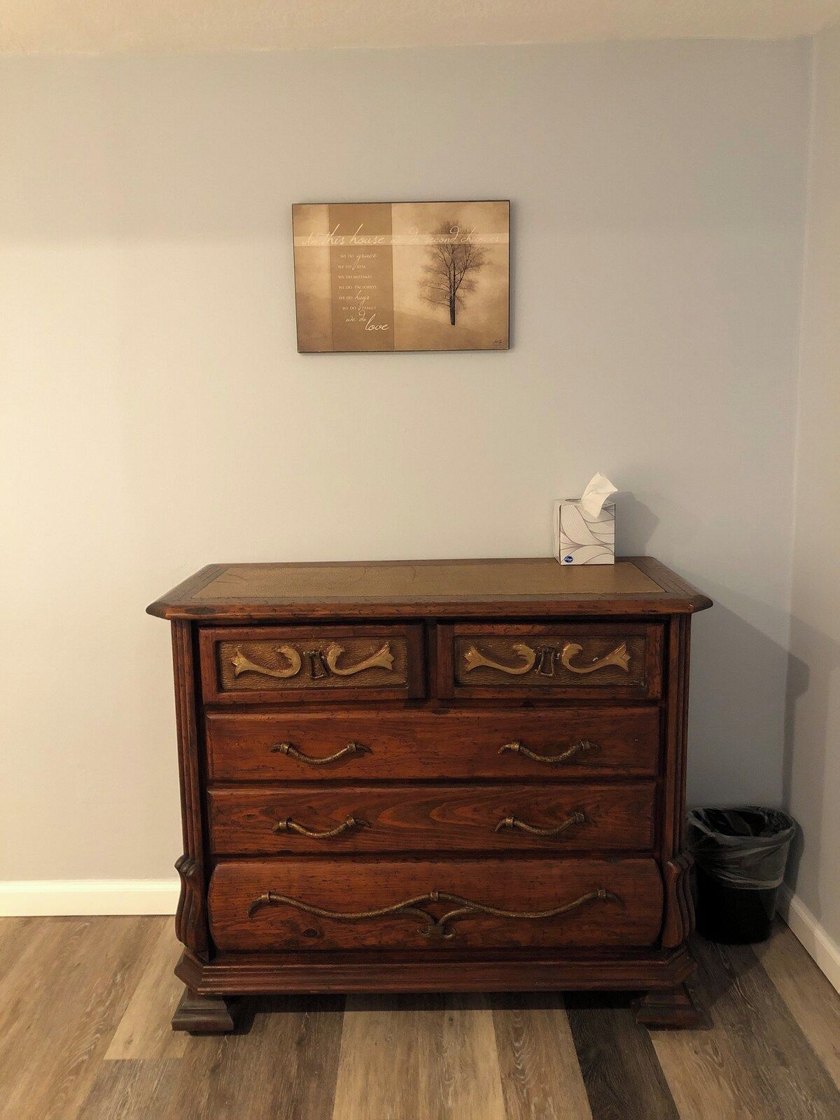 A wooden dresser with brass handles and a framed quote on the wall above it.
