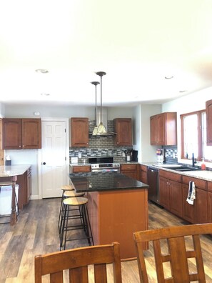 A kitchen with a central island, wooden cabinets, a built-in oven, and a hanging light fixture.