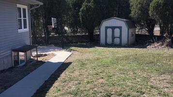A residential backyard with a house, a shed, a basketball hoop, and a concrete pathway.