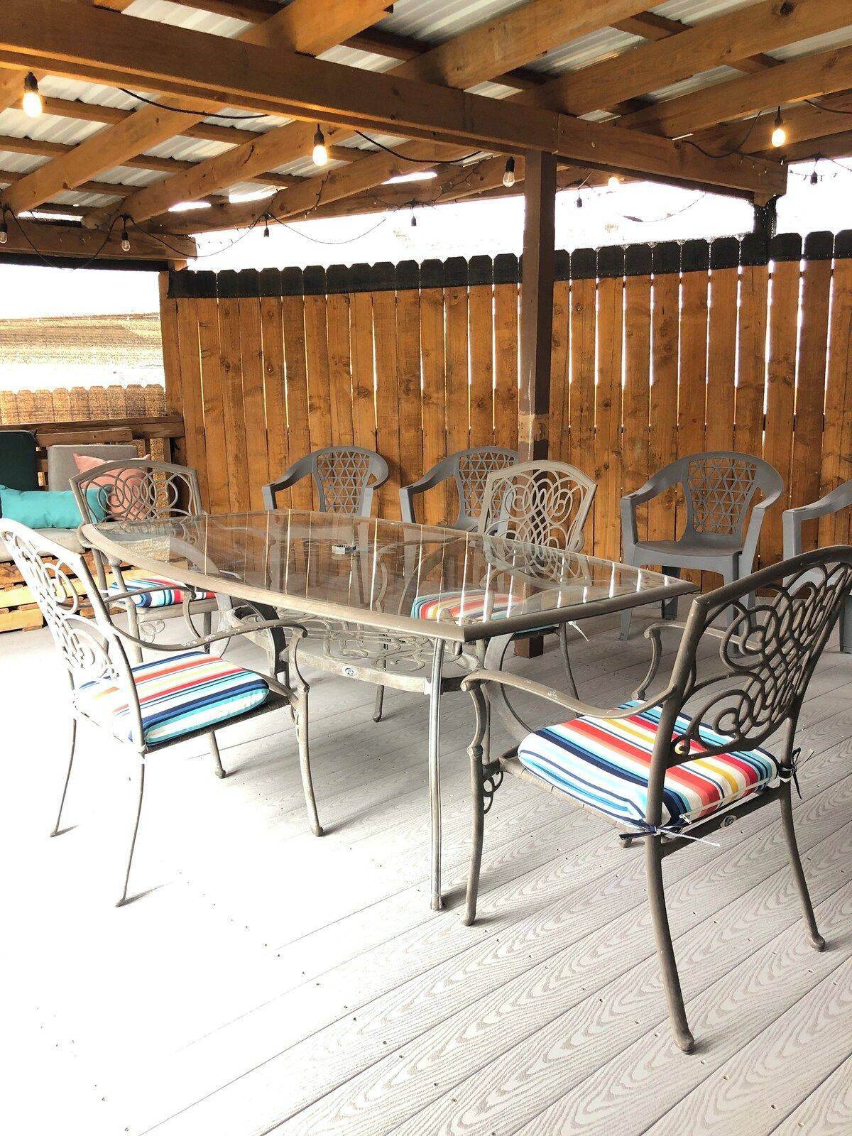 A covered patio area with a glass-top table and metal chairs with colorful cushions.