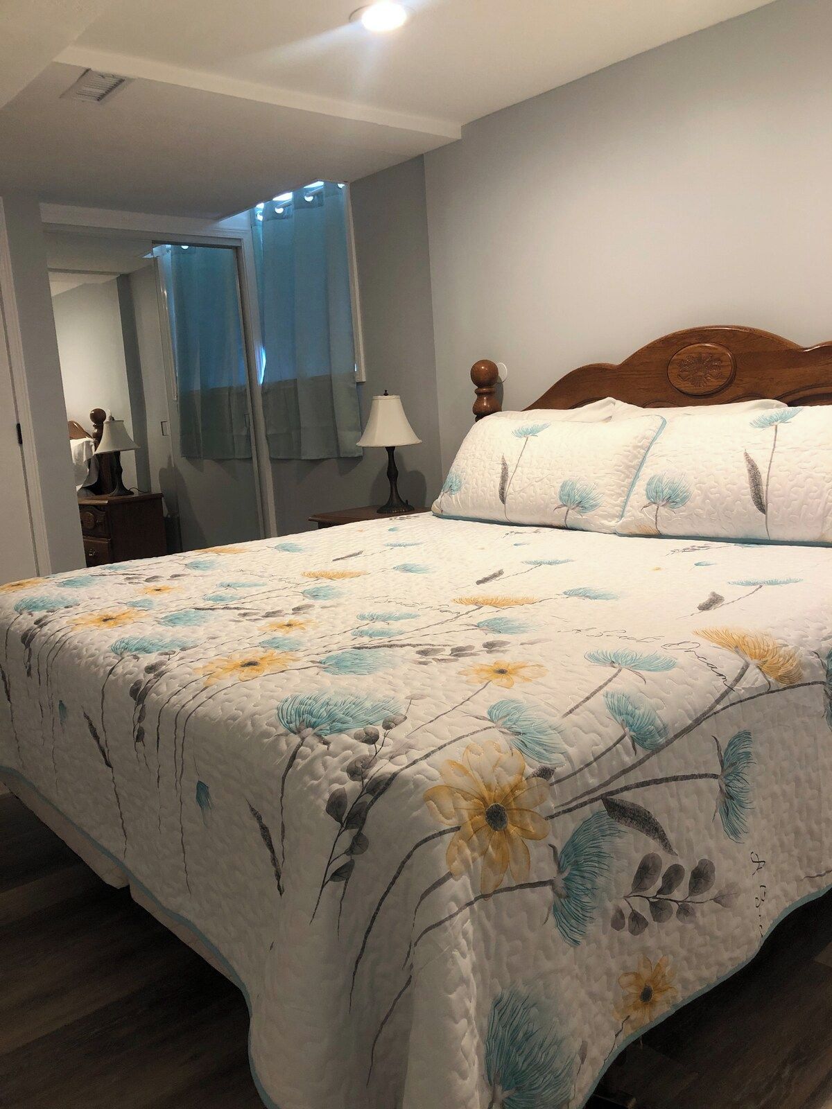 A bedroom with a bed, a nightstand, a lamp, a mirror, and a window with curtains.