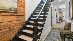 Un escalier avec des marches en bois et des balustrades noires, menant à un palier agrémenté d’un tapis et d’un banc.