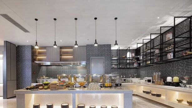 A modern kitchen with a central island, pendant lighting, and brick-patterned walls. - Wanda Yue Hotel Bengbu South Station (Bengbu)