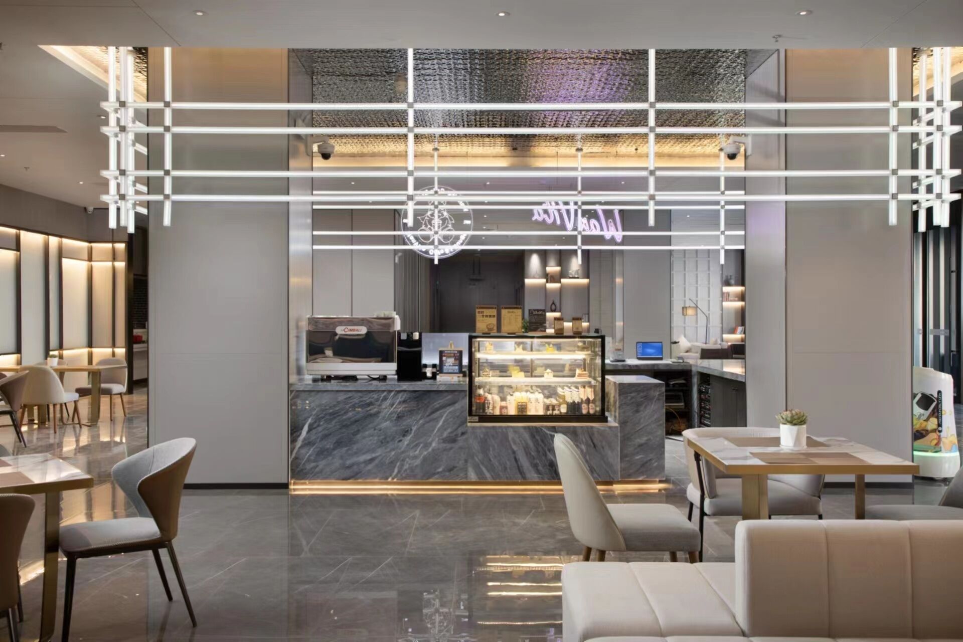 A modern hotel lobby with a reception desk, seating area, and a coffee bar.