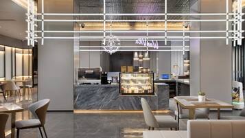 A modern hotel lobby with a reception desk, seating area, and a coffee bar.