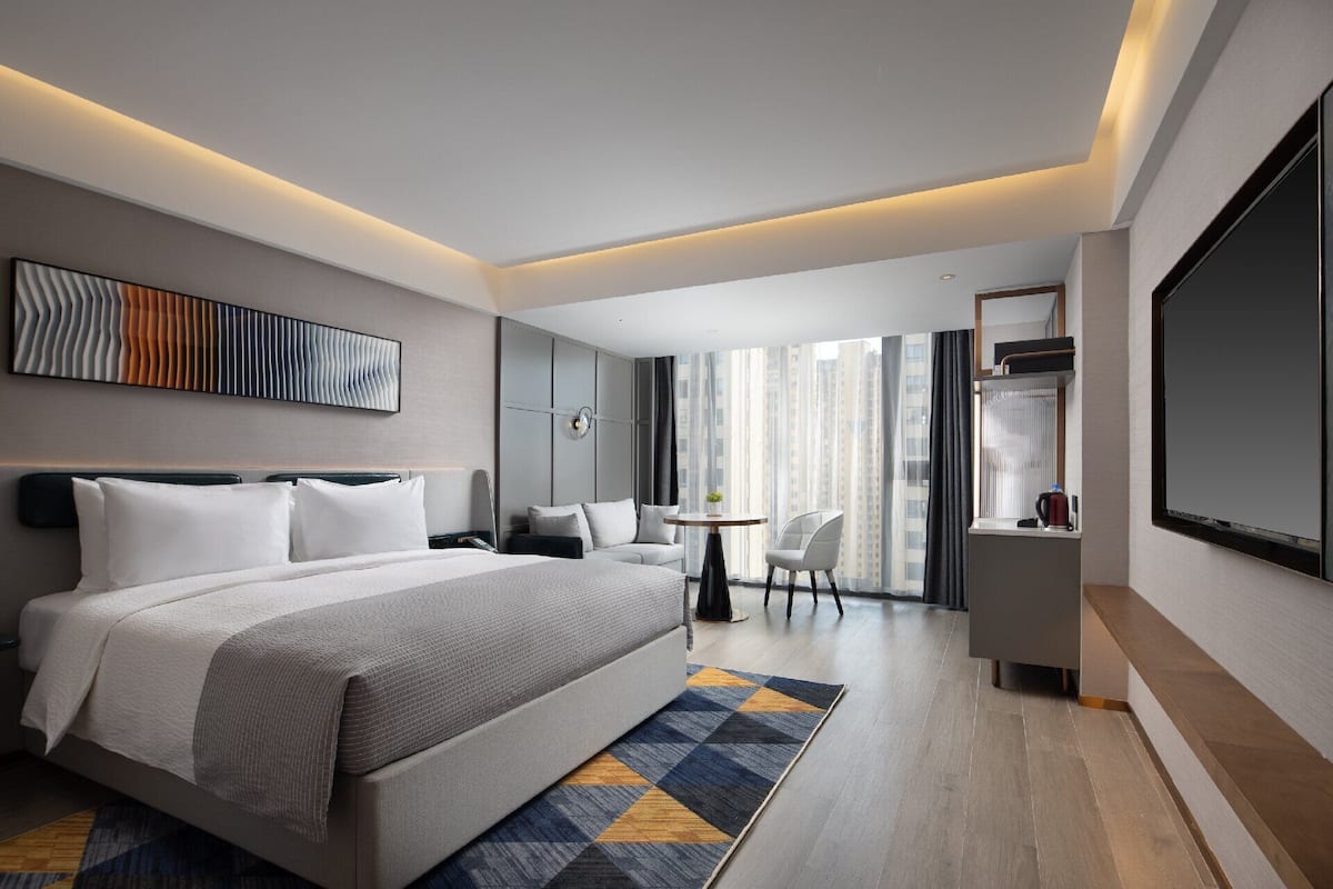 A modern hotel room with a large bed, a desk, a chair, and a TV.