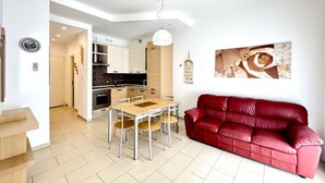 A modern kitchen with white cabinets, a dining table with chairs, and a red leather sofa in a bright living area.