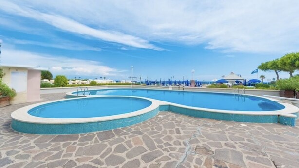 A swimming pool with a stone deck, surrounded by umbrellas and lounge chairs.
