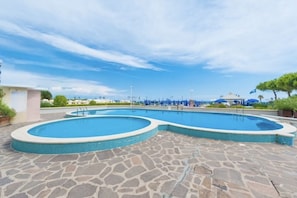 Une piscine entourée d’un sol en pierre, de parasols et de chaises longues.