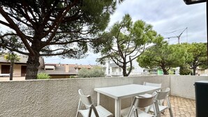 An outdoor patio with a white table and four chairs, surrounded by a low wall and trees.