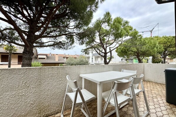 An outdoor patio with a white table and four chairs, surrounded by a low wall and trees.