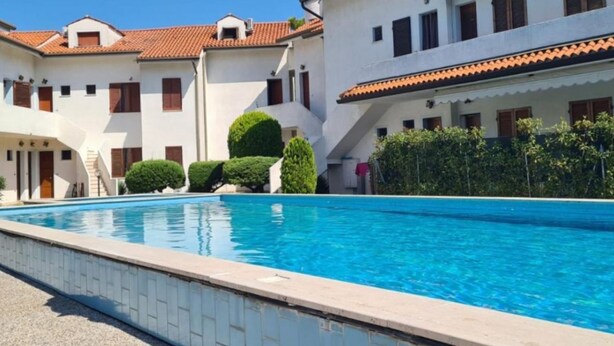 A swimming pool with a clear blue water surface, surrounded by white buildings with red-tiled roofs and multiple windows.