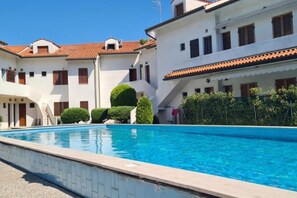 A swimming pool with a clear blue water surface, surrounded by white buildings with red-tiled roofs and multiple windows.