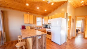 A kitchen with wooden cabinets, a central island with stools, a refrigerator, and a stove. - Cabin 2 steps from the water (Isle)