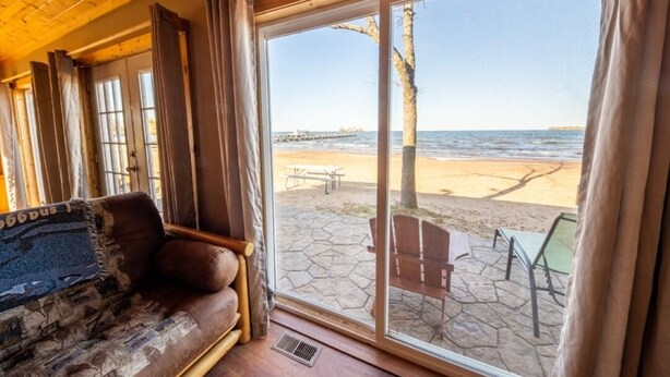 A cozy room with a large window overlooking a beach, a wooden ceiling, and a comfortable seating area. - 3 Bedroom Cabin 3 Beach front (Isle)