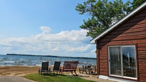 A wooden cabin with a large sliding glass door, a patio with outdoor seating, and a view of the lake. - 3 Bedroom Cabin 3 Beach front (Isle)