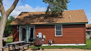 A rustic wooden cabin with a green door, a picnic table, and a barbecue grill. - Cabin 4 at the Lake - 2 bedrooms (Isle)