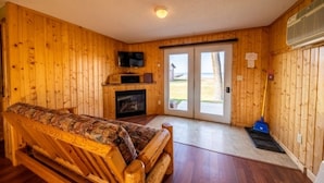 A wooden interior with a sofa, television, fireplace, and a view through a sliding door. - Cabin 4 at the Lake - 2 bedrooms (Isle)