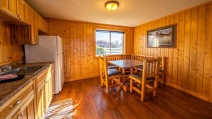 A wooden-paneled kitchen with a dining table and chairs, a refrigerator, and a window with a view. - Cabin 4 at the Lake - 2 bedrooms (Isle)