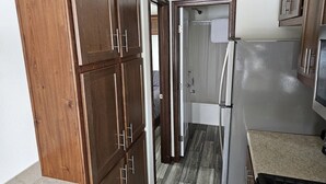 Una cocina compacta con armarios de madera, un refrigerador y una zona de ducha visible a través de una puerta abierta.
