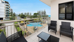 Un balcón con piscina, mobiliario exterior y vistas a una zona residencial y al océano.