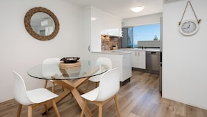 Una cocina moderna con armarios blancos, una mesa de comedor de vidrio y una pared de ladrillo decorativa.