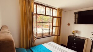 Une chambre à coucher comprenant un lit, un bureau, une chaise, un téléviseur et une fenêtre avec des rideaux.