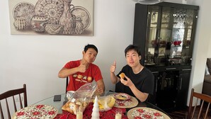 Une table à manger recouverte d’une nappe rouge, avec des assiettes et un verre de lait. Des chaises sont disposées autour de la table, et une personne est assise à la table, levant le pouce en signe d’approbation.