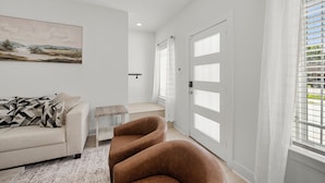 Un salon moderne avec un canapé, un fauteuil marron, un tableau au mur et une porte avec une fenêtre.