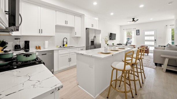 Une cuisine moderne avec des meubles blancs, un îlot central doté de tabourets, une cuisinière et un réfrigérateur.