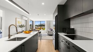 A modern kitchen with a large island, black cabinetry, and a view of the outdoors. - Mountainview Escape | Stylish, BBQ, and Parking (Wānaka)