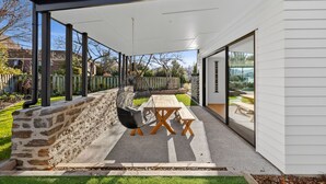 Un patio couvert avec une table et des chaises, un fauteuil suspendu et un mur en pierre.