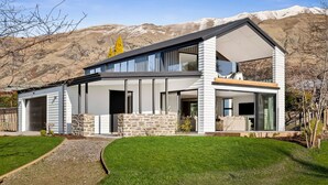 Une maison moderne à deux étages, dotée d’une façade en pierre, de grandes fenêtres et d’un toit plat.