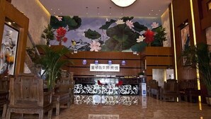 Eine Lobby mit einem Chandelier, Holzmöbeln und einem Wandgemälde von Lotusblumen und Vögeln.